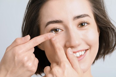 Photo of Woman putting in contact lens on light background, closeup