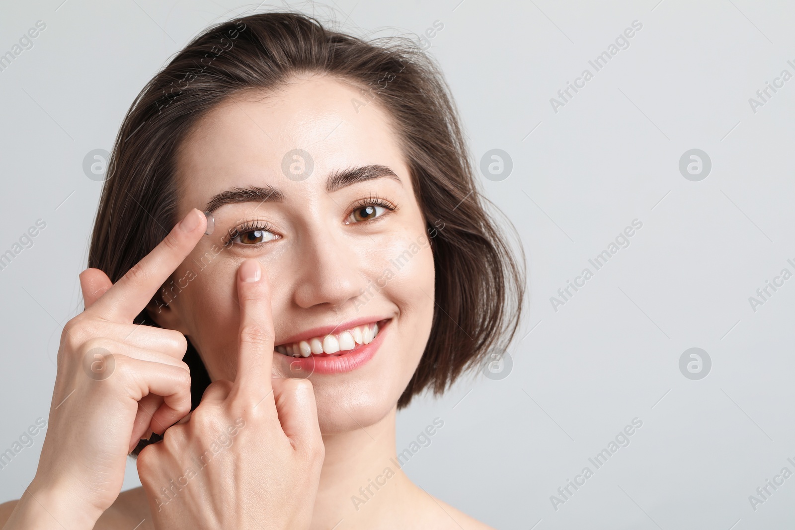 Woman putting in contact lens on light background. Space for text Photo of Woman putting in contact lens on light background. Space for text