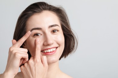 Photo of Woman putting in contact lens on light background. Space for text