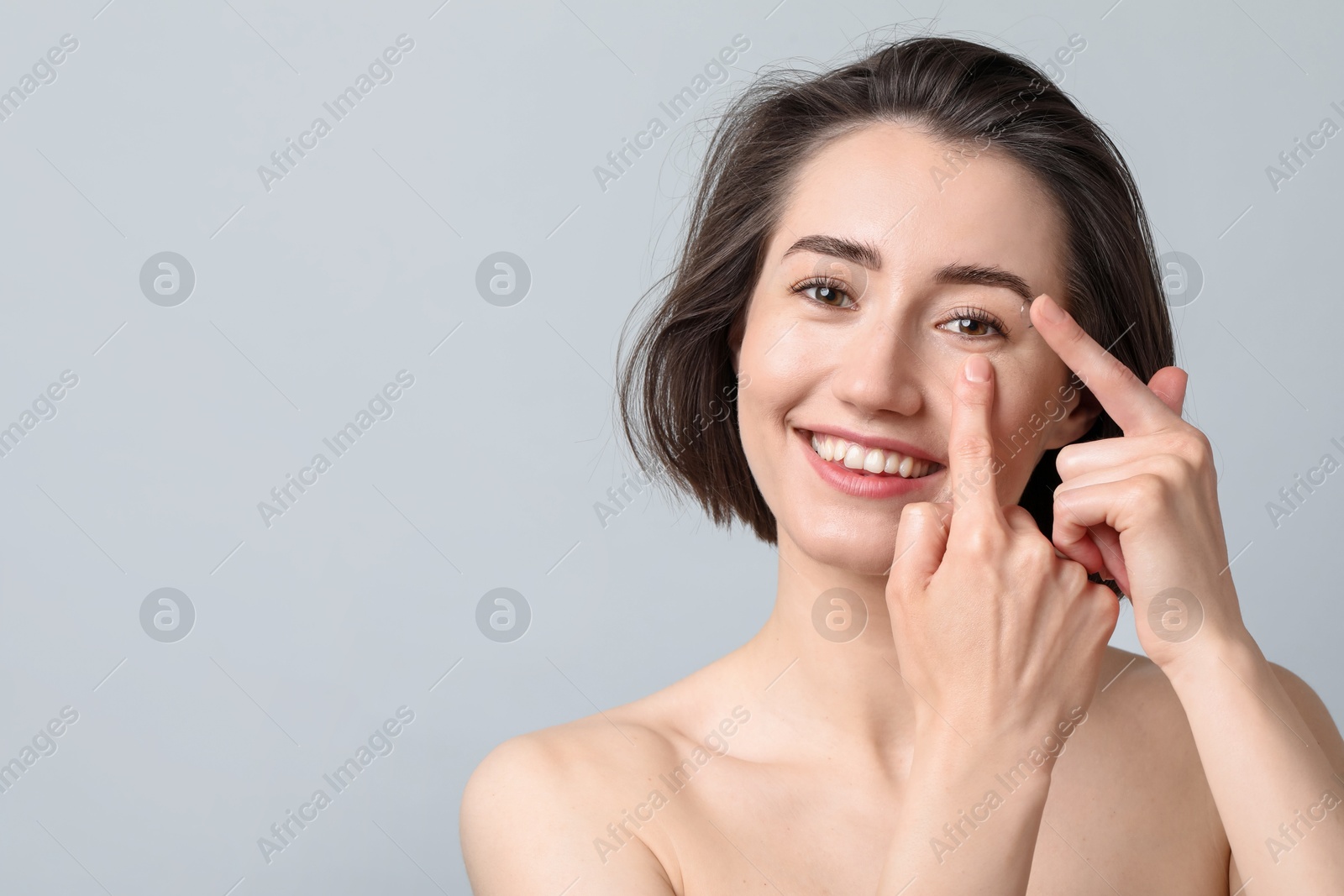 Woman putting in contact lens on light background. Space for text Photo of Woman putting in contact lens on light background. Space for text