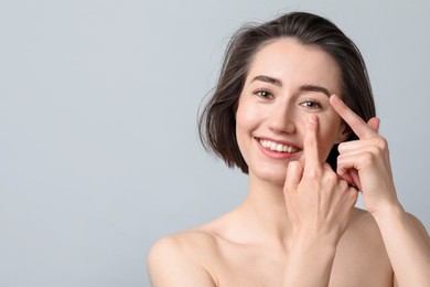 Photo of Woman putting in contact lens on light background. Space for text