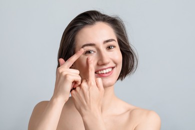 Photo of Woman putting in contact lens on light background