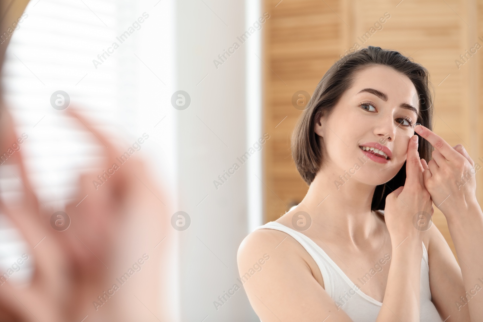 Woman putting in contact lens near mirror indoors Photo of Woman putting in contact lens near mirror indoors