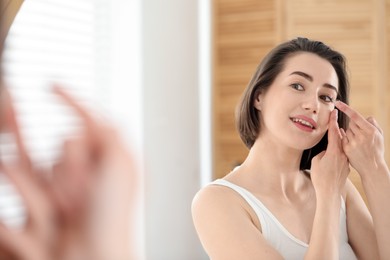Photo of Woman putting in contact lens near mirror indoors