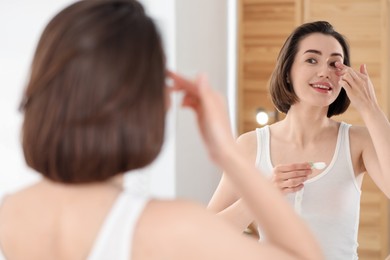 Photo of Woman putting in contact lens near mirror indoors