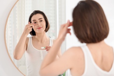 Photo of Woman putting in contact lens near mirror indoors