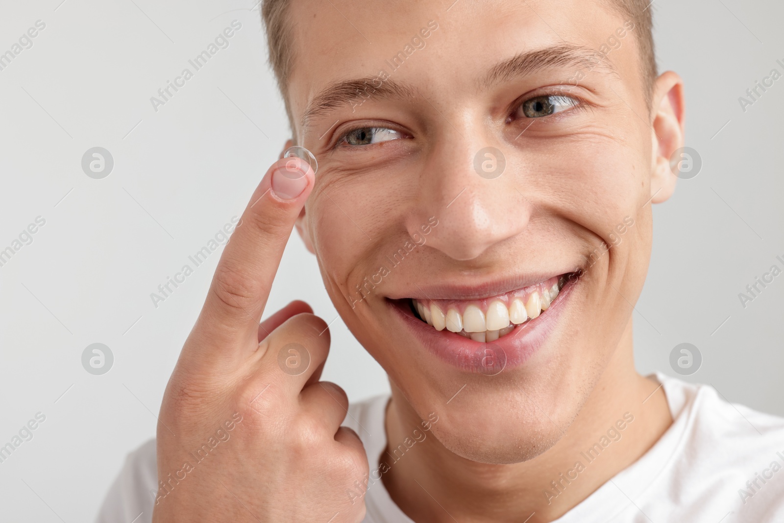 Photo of Man putting in contact lens on light background, closeup