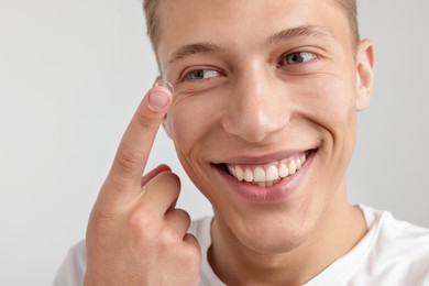 Photo of Man putting in contact lens on light background, closeup