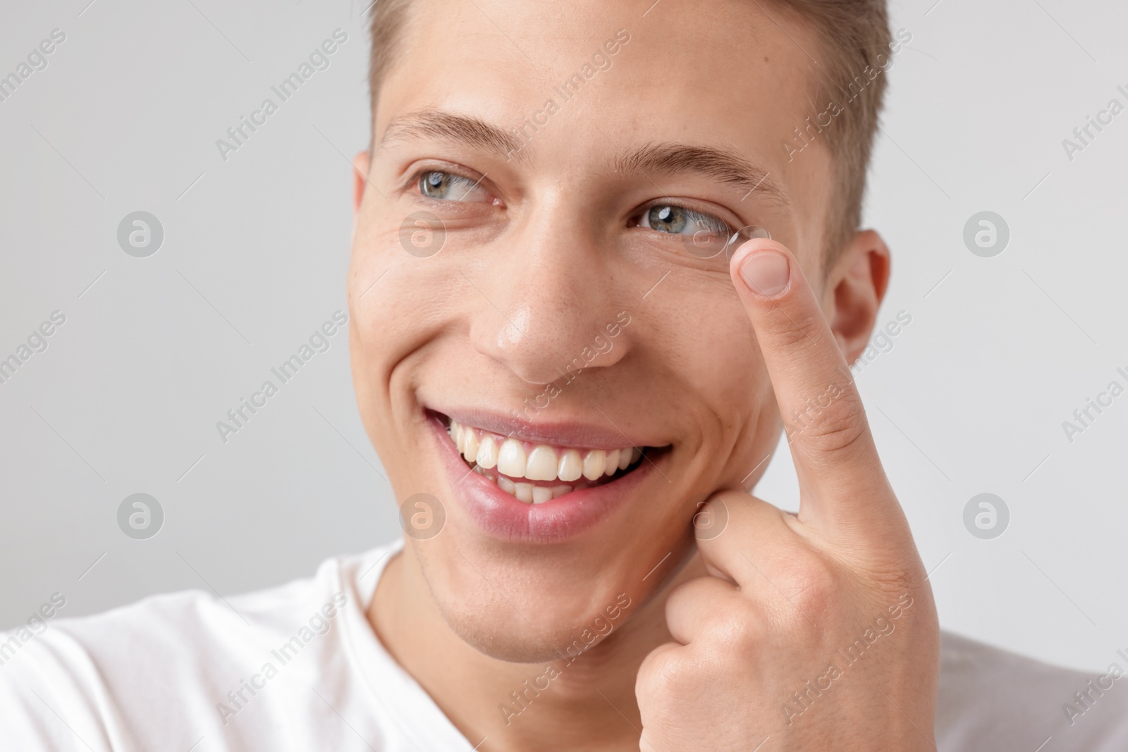 Photo of Man putting in contact lens on light background, closeup