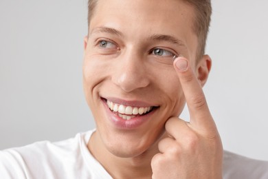 Photo of Man putting in contact lens on light background, closeup