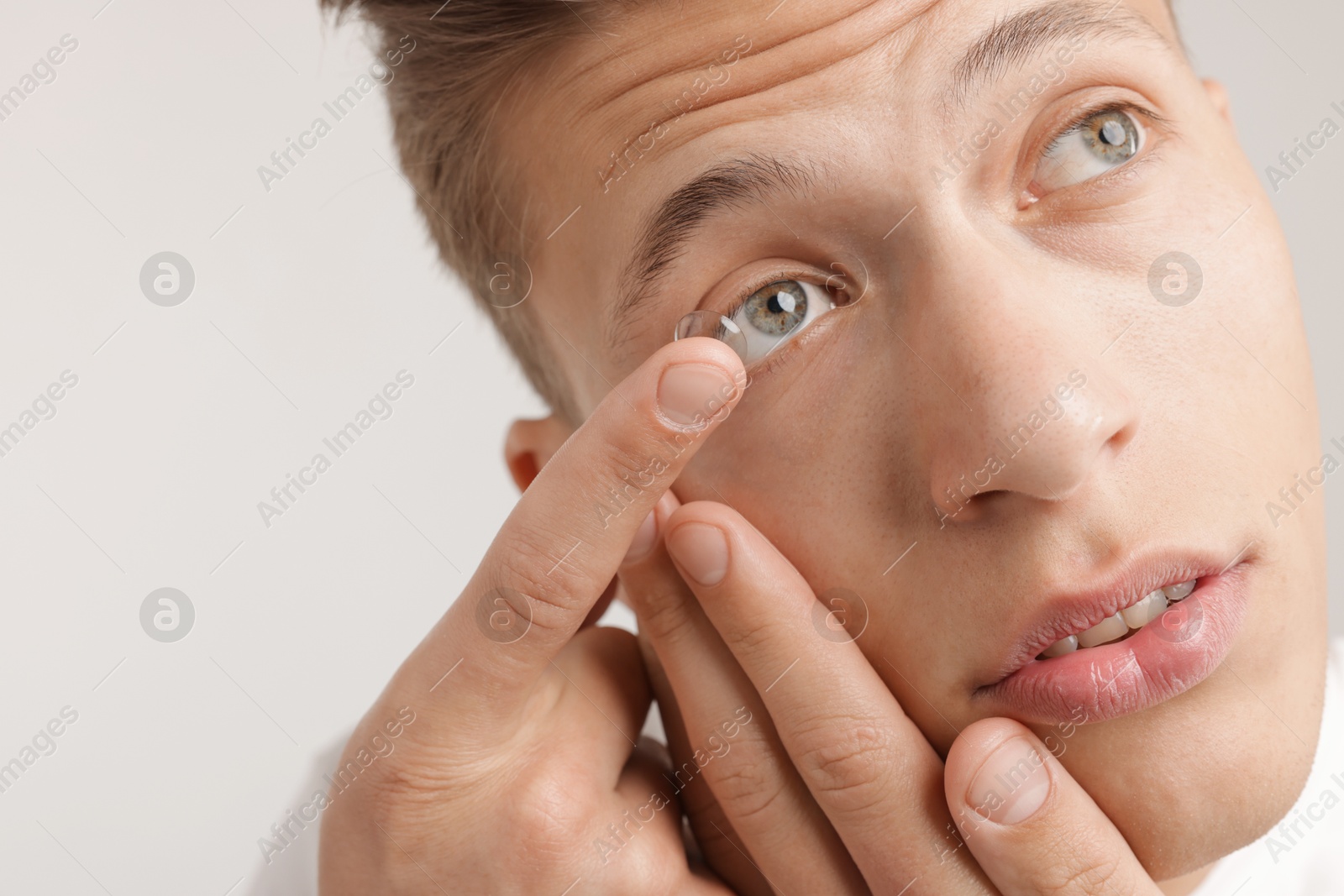 Photo of Man putting in contact lens on light background, closeup