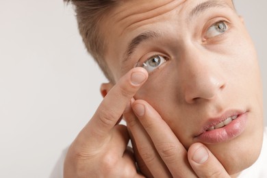 Photo of Man putting in contact lens on light background, closeup