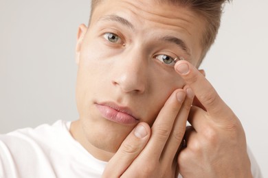 Photo of Man putting in contact lens on light background, closeup