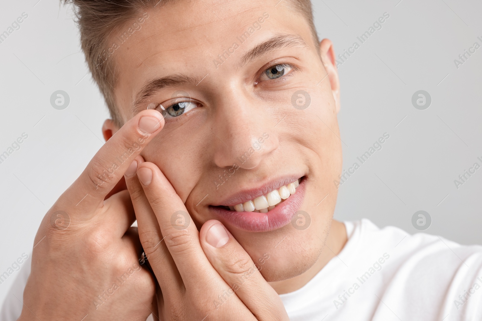 Photo of Man putting in contact lens on light background, closeup