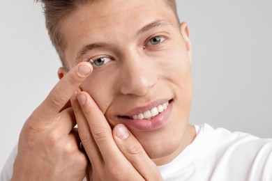 Photo of Man putting in contact lens on light background, closeup