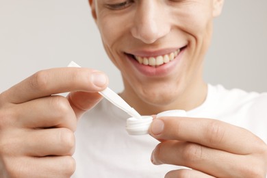 Photo of Man taking contact lens out of case on light background, closeup