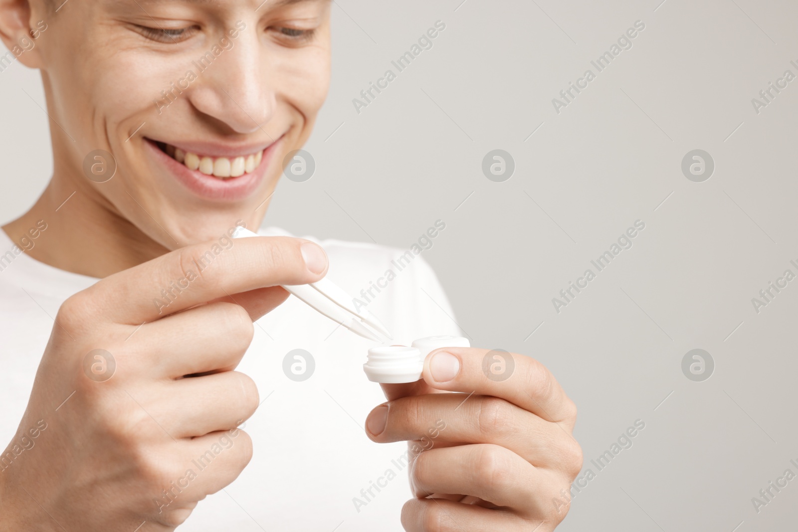 Photo of Man taking contact lens out of case on light background, closeup. Space for text