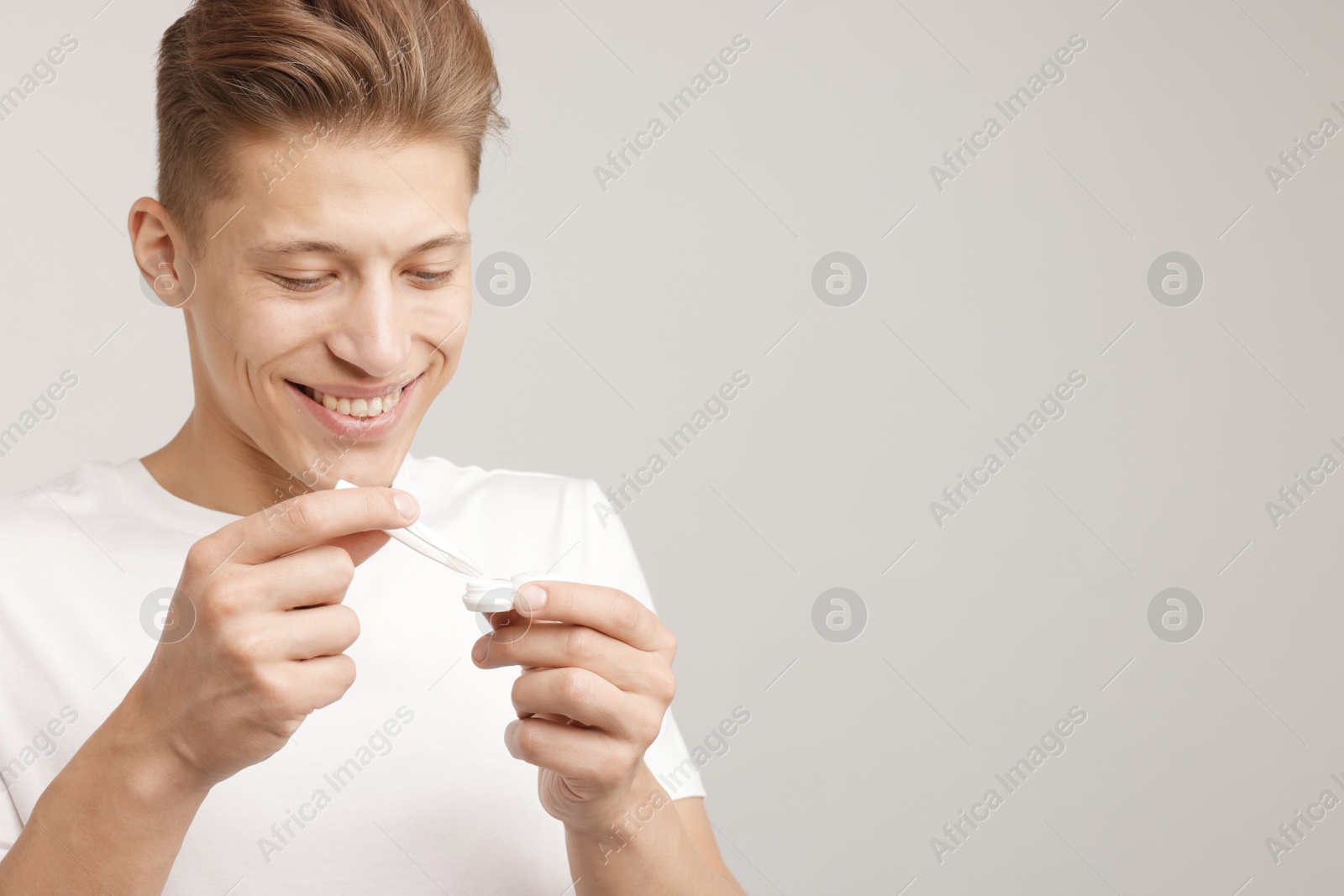 Photo of Man taking contact lens out of case on light background. Space for text