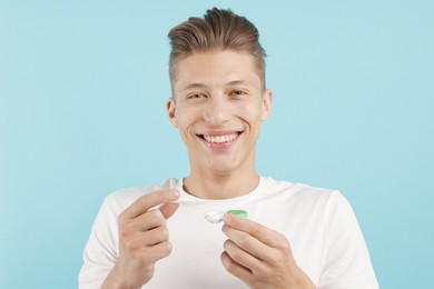 Photo of Man taking contact lens out of case on light blue background