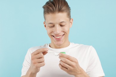 Photo of Man taking contact lens out of case on light blue background
