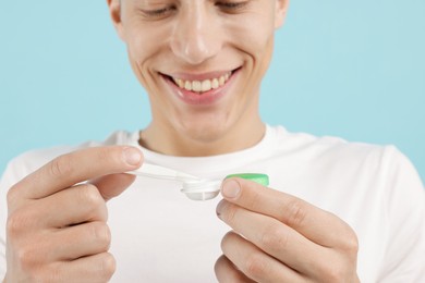Photo of Man taking contact lens out of case on light blue background, closeup