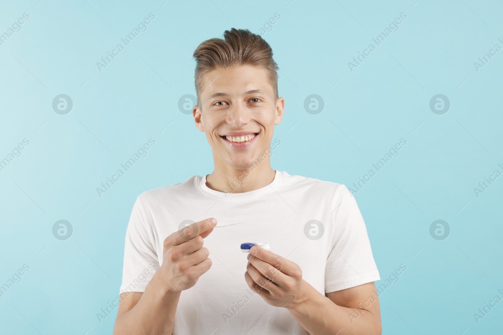 Man with contact lens and case on light blue background Photo of Man with contact lens and case on light blue background