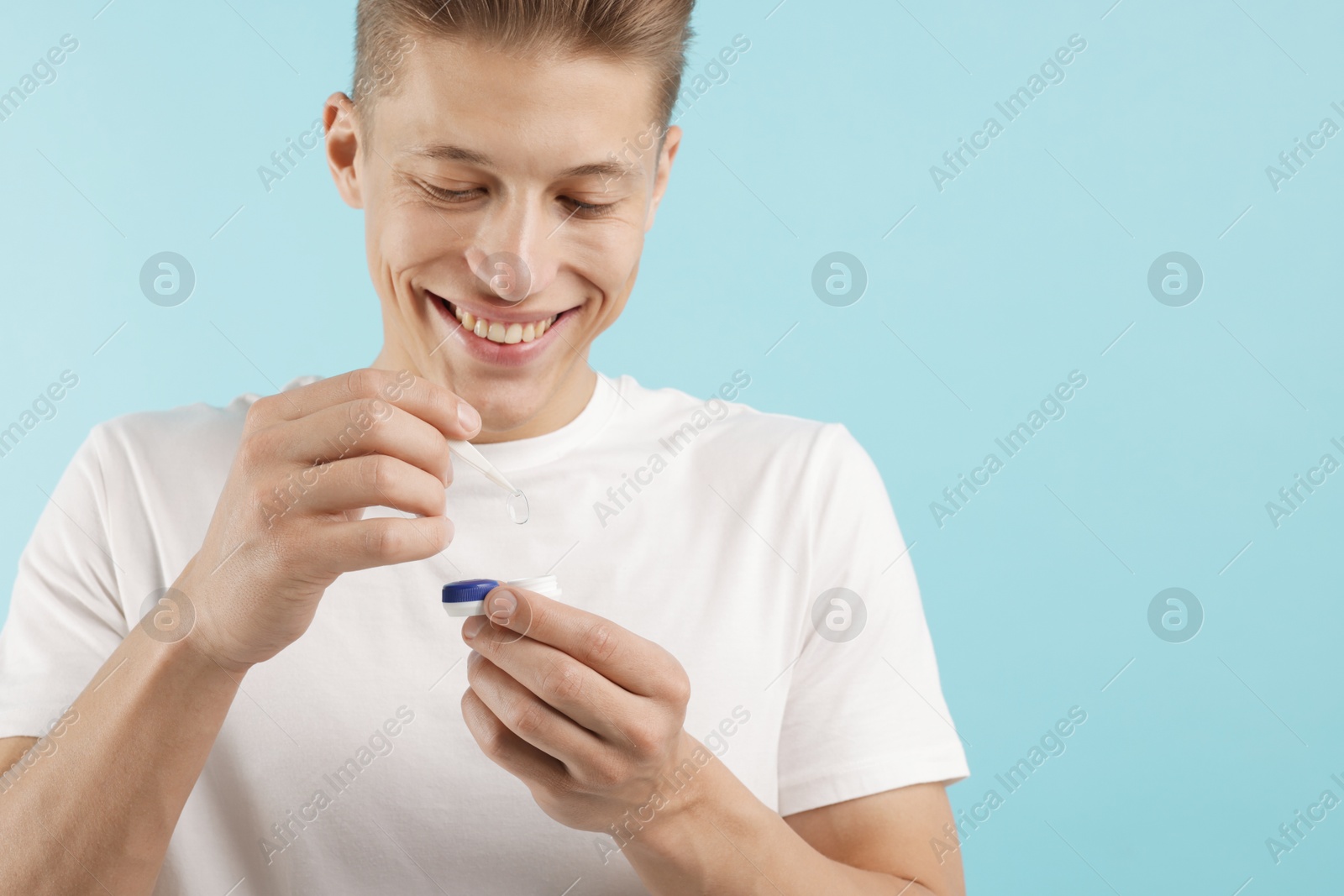 Man taking contact lens out of case on light blue background Photo of Man taking contact lens out of case on light blue background