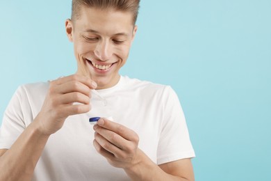 Photo of Man taking contact lens out of case on light blue background
