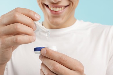 Photo of Man taking contact lens out of case on light blue background, closeup