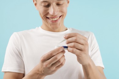 Photo of Man taking contact lens out of case on light blue background, closeup