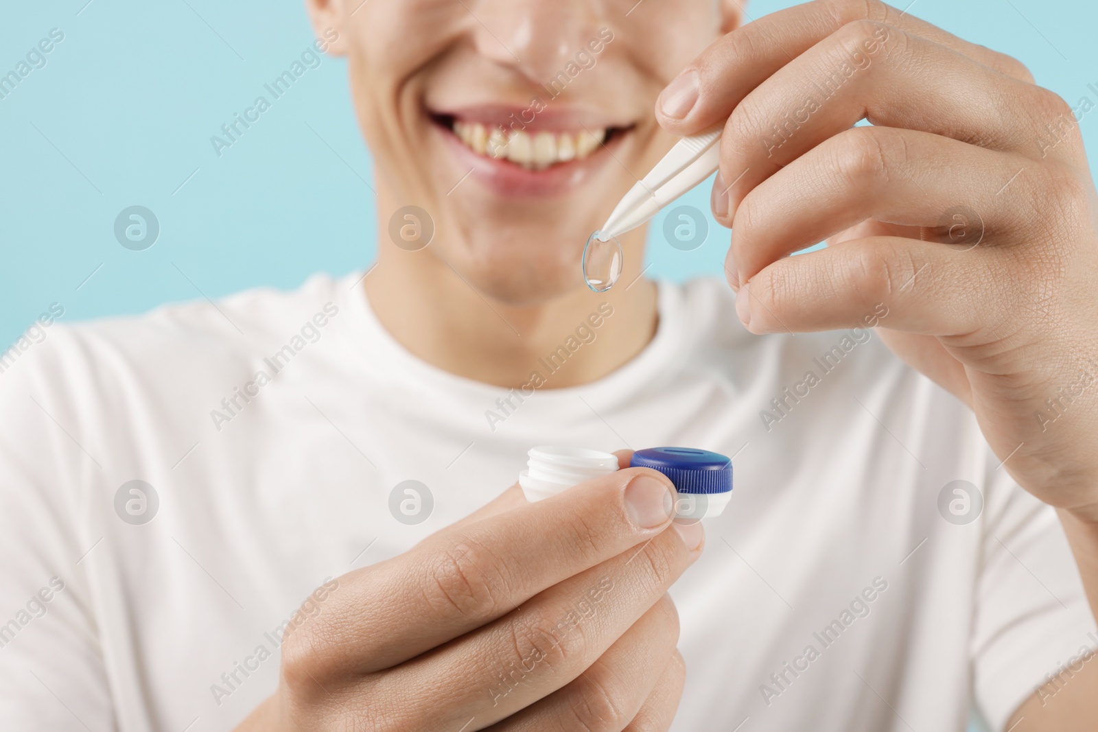 Man taking contact lens out of case on light blue background, closeup Photo of Man taking contact lens out of case on light blue background, closeup
