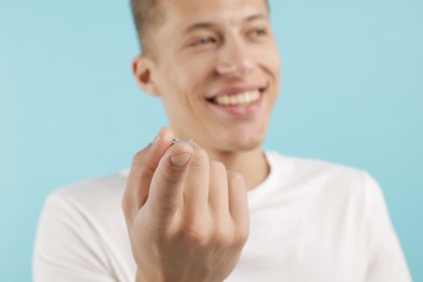 Photo of Man with contact lens on light blue background, selective focus