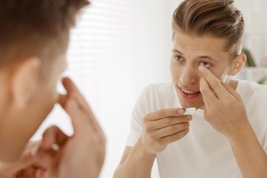 Photo of Man putting in contact lens near mirror at home
