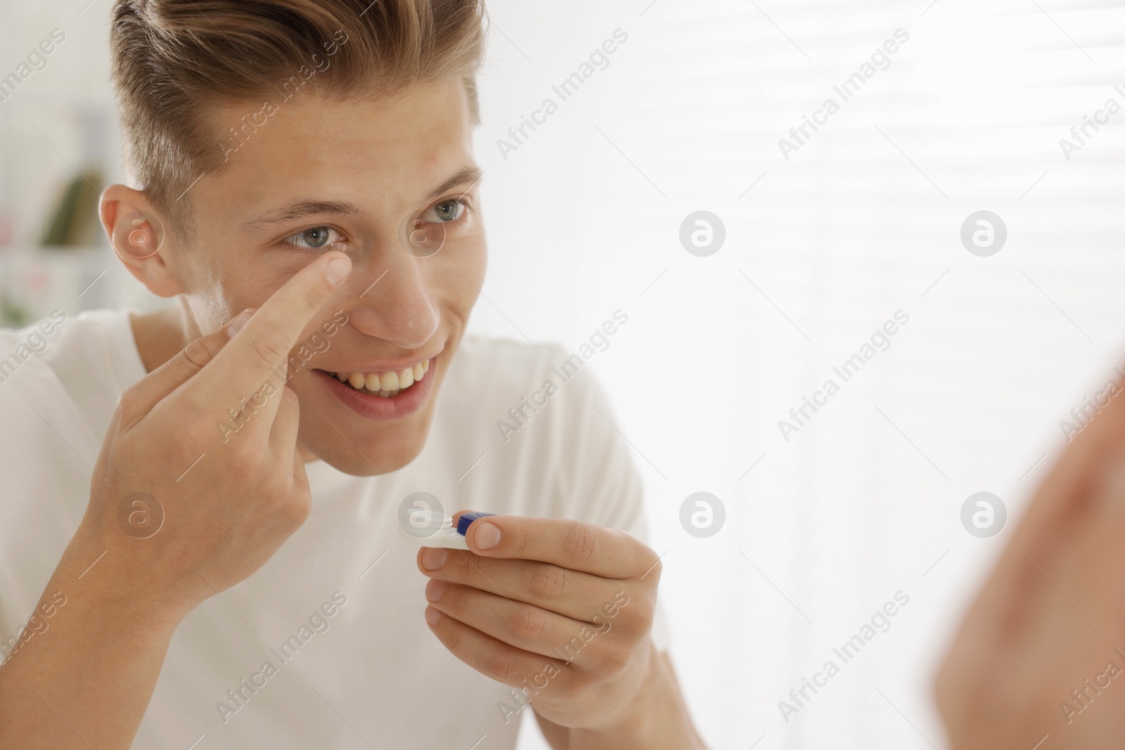 Man putting in contact lens near mirror at home. Space for text Photo of Man putting in contact lens near mirror at home. Space for text