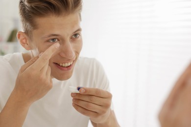 Photo of Man putting in contact lens near mirror at home. Space for text