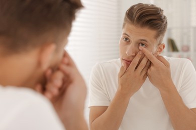 Photo of Man putting in contact lens near mirror at home