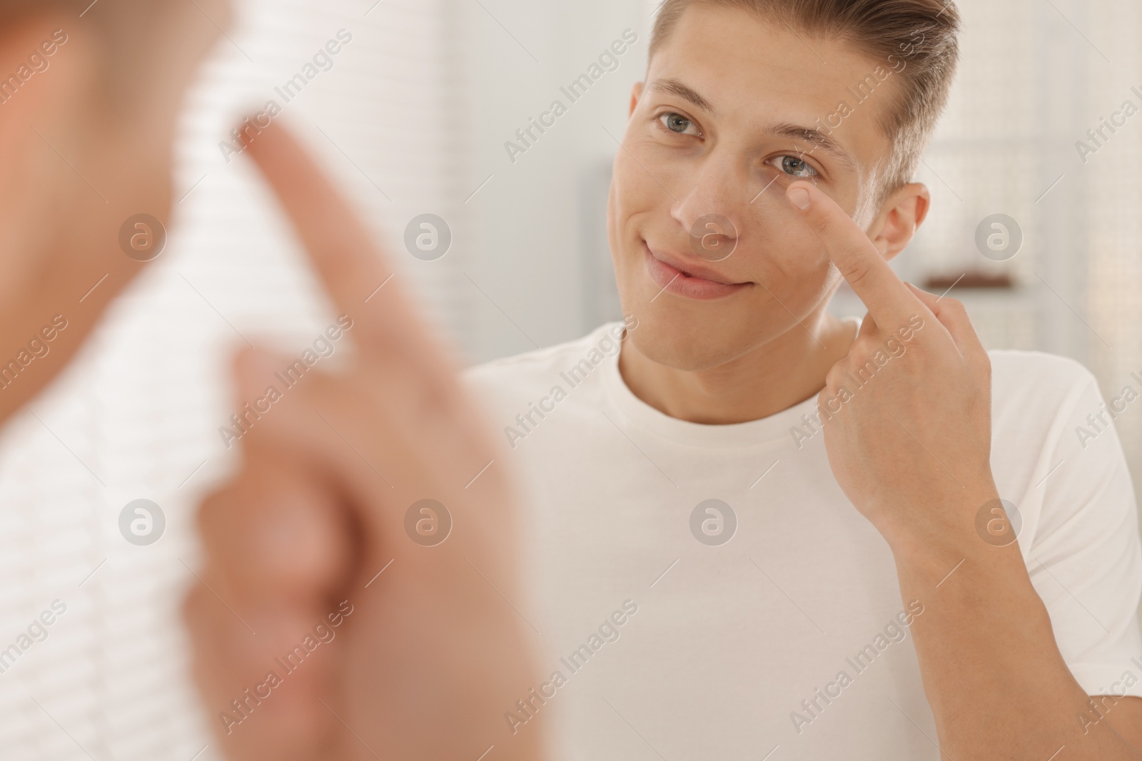 Man putting in contact lens near mirror at home Photo of Man putting in contact lens near mirror at home