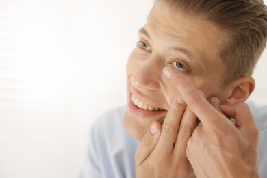 Photo of Man putting in contact lens at home. Space for text