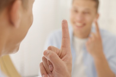 Photo of Man with contact lens near mirror at home, selective focus