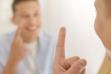 Photo of Man with contact lens near mirror at home, selective focus