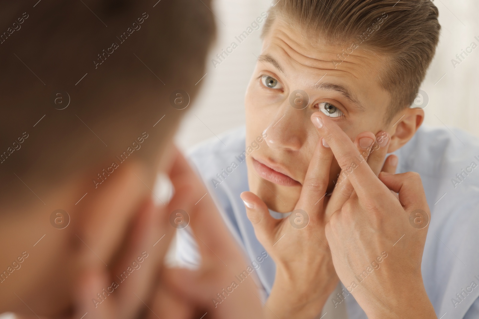 Man putting in contact lens near mirror at home, closeup Photo of Man putting in contact lens near mirror at home, closeup
