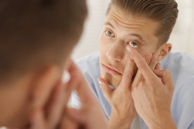 Photo of Man putting in contact lens near mirror at home, closeup
