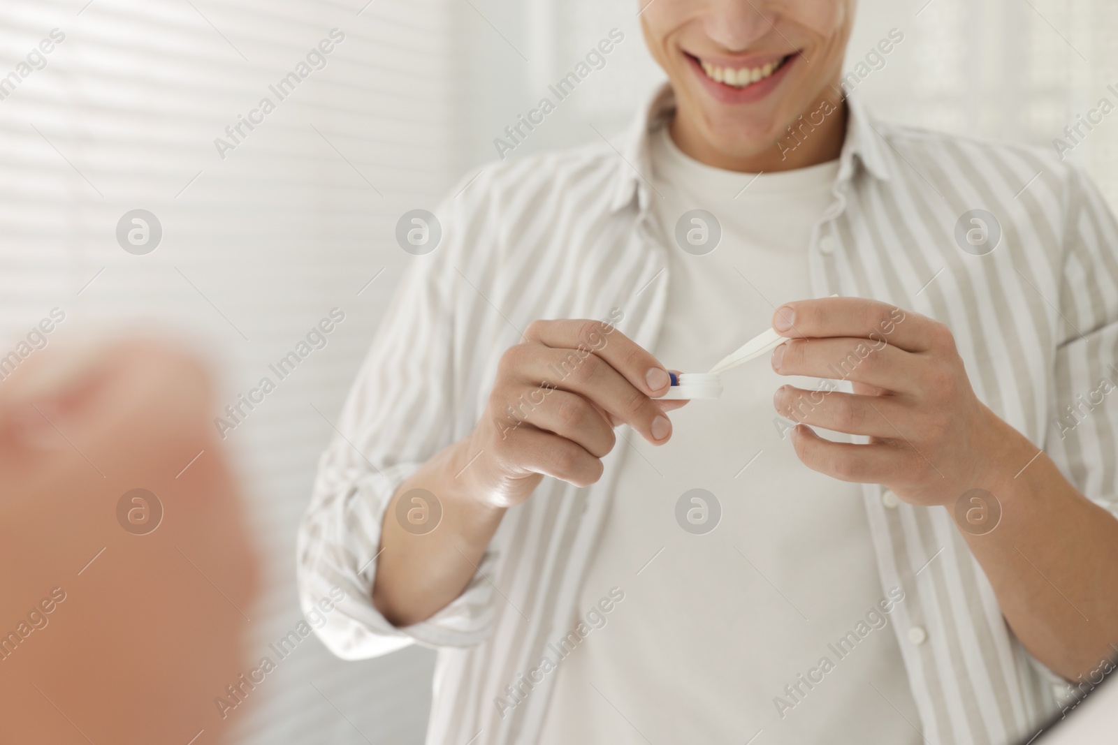 Photo of Man taking contact lens out of case near mirror at home, closeup