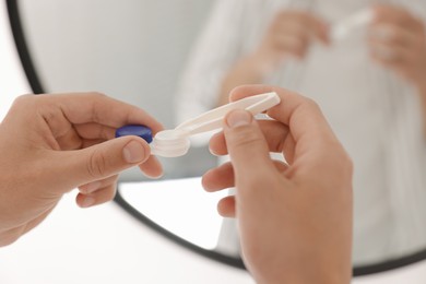 Photo of Man taking contact lens out of case near mirror at home, closeup