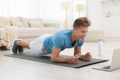Photo of Man doing plank exercise during online class with coach at home. Sport and healthy lifestyle
