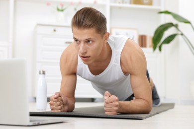 Photo of Man doing plank exercise during online class with coach at home. Sport and healthy lifestyle