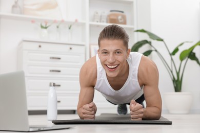 Photo of Man doing plank exercise during online class with coach at home. Sport and healthy lifestyle