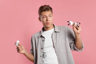 Photo of Man choosing between glasses and contact lenses on pink background