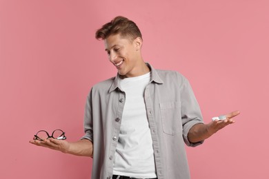 Photo of Man choosing between glasses and contact lenses on pink background