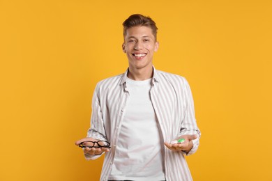 Photo of Man choosing between glasses and contact lenses on yellow background
